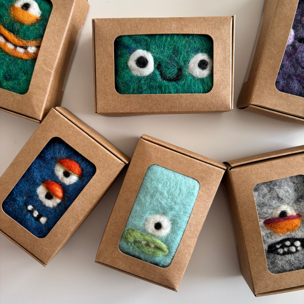Small felted toys with facial expressions in brown boxes on a light background