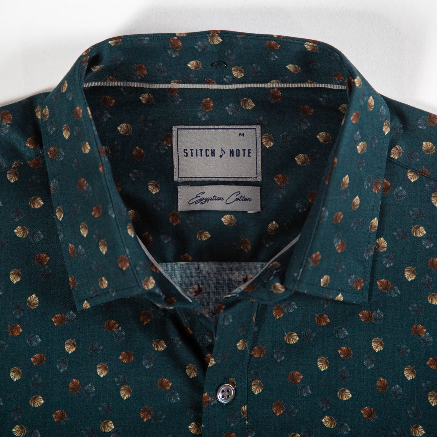 Teal shirt with gold leaf pattern and Stitch & Note label on a white background
