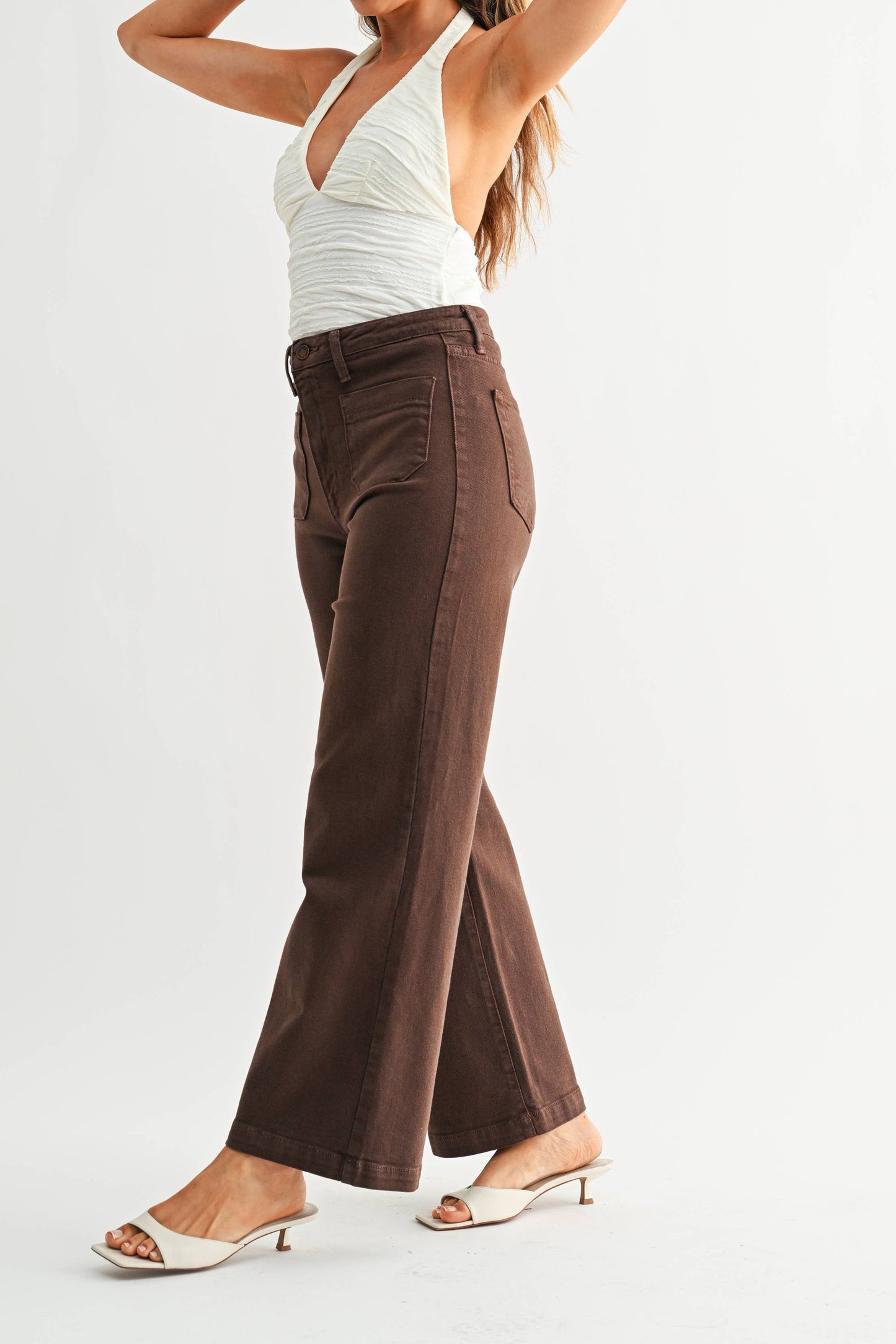 Woman wearing a white top and brown high-waisted pants on a light gray background
