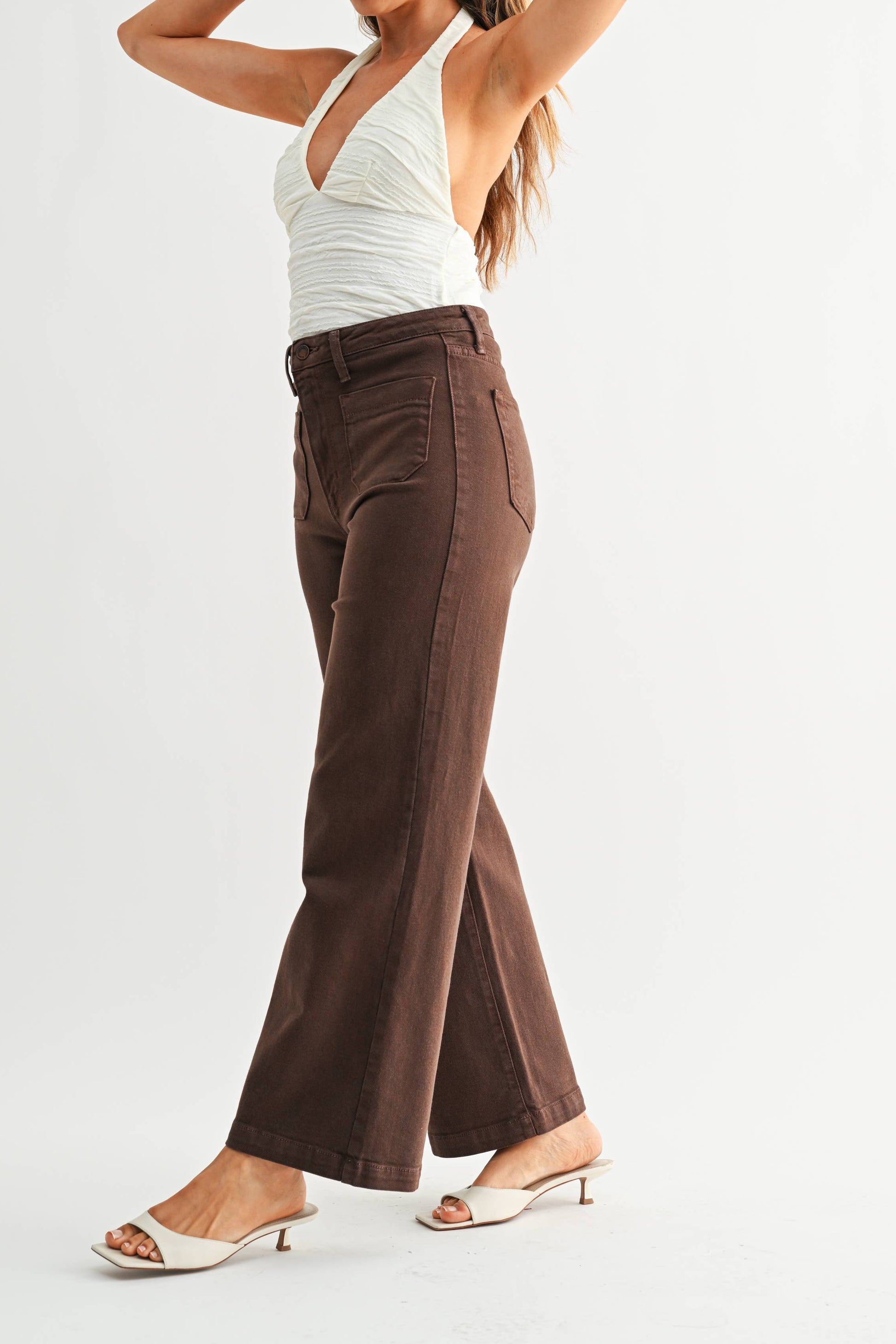 Woman wearing a white top and brown high-waisted pants on a light gray background