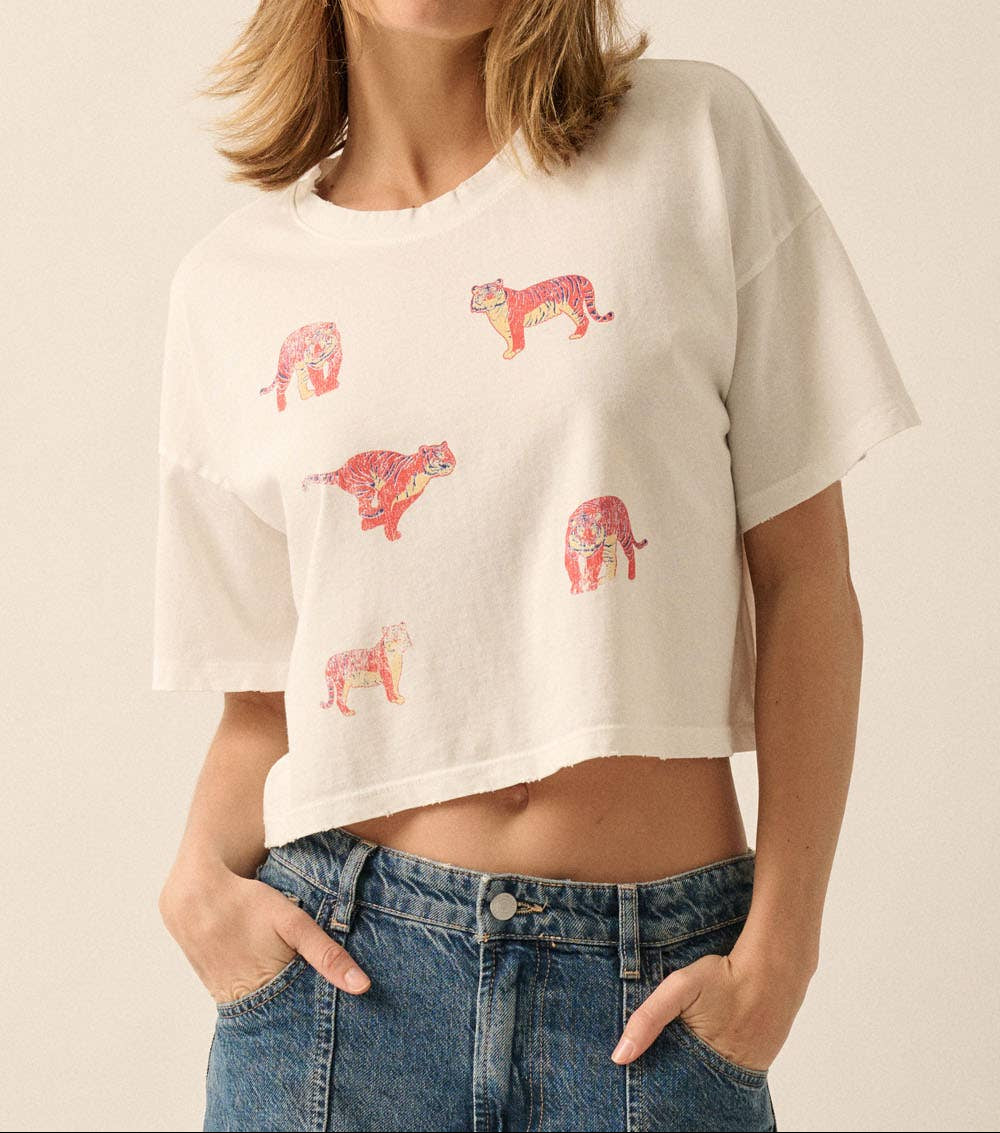 A woman wearing a cropped off-white t-shirt with pink and red leopard prints, paired with blue jeans, against a plain beige background.