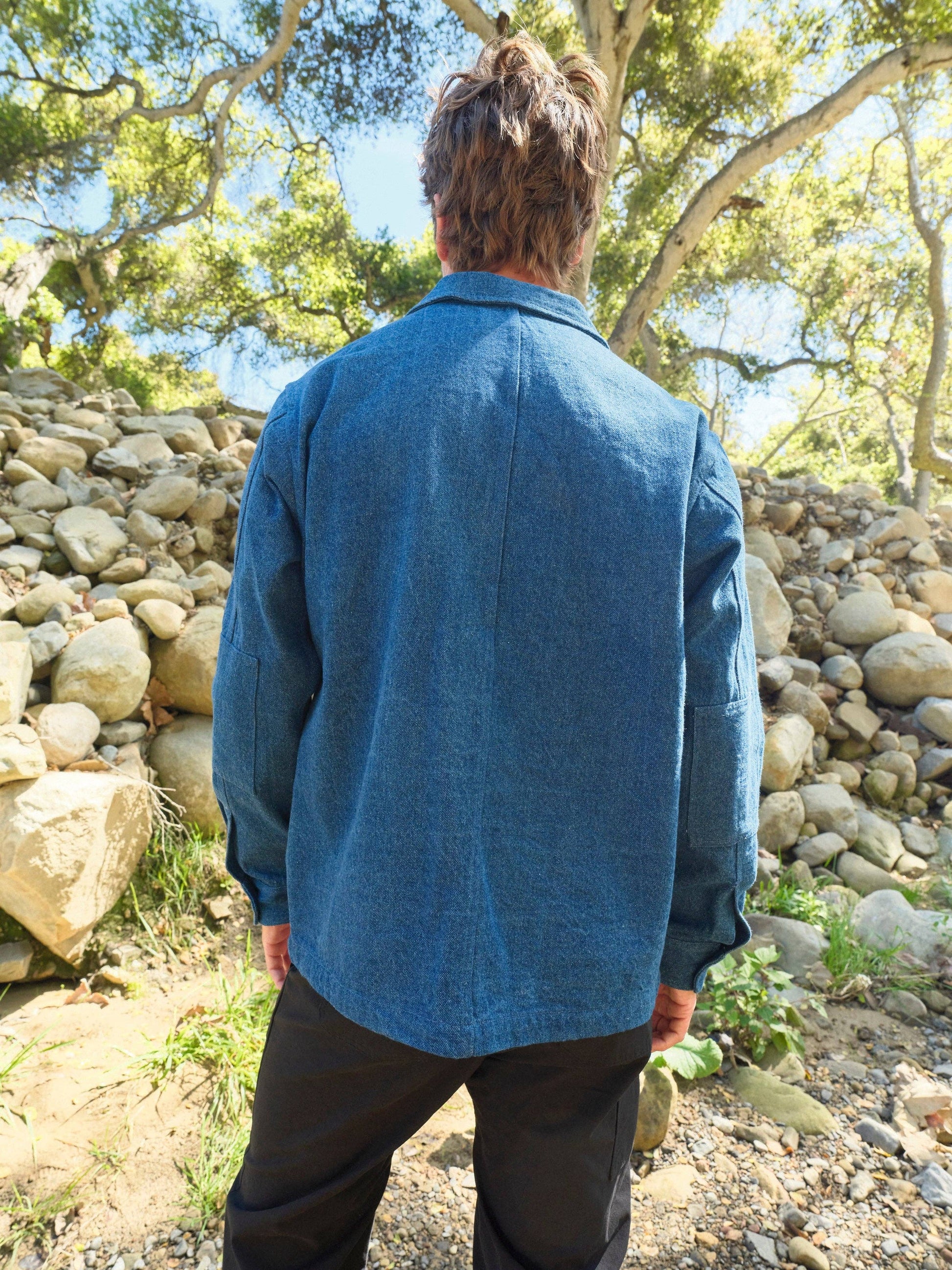 Person wearing a blue jacket standing in a natural setting with trees and rocks.