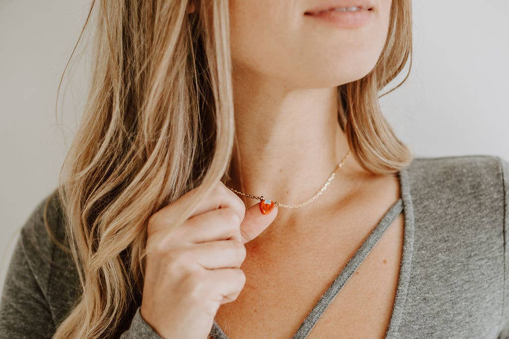 Person wearing a necklace with a heart pendant, holding it close to their chest.