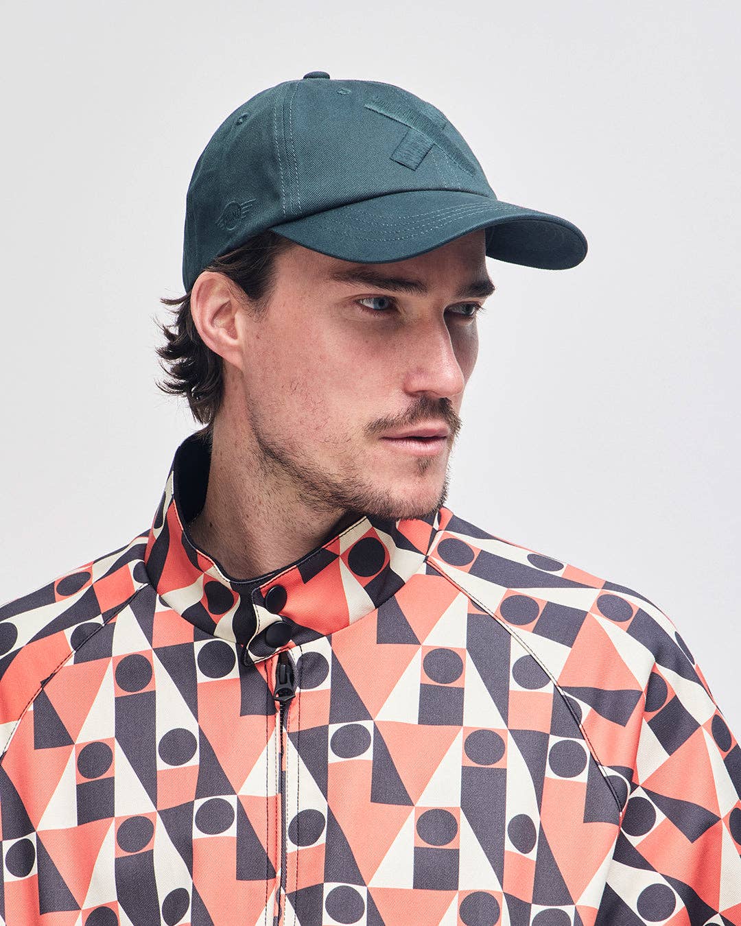 Man wearing a patterned jacket and green cap against a light gray background