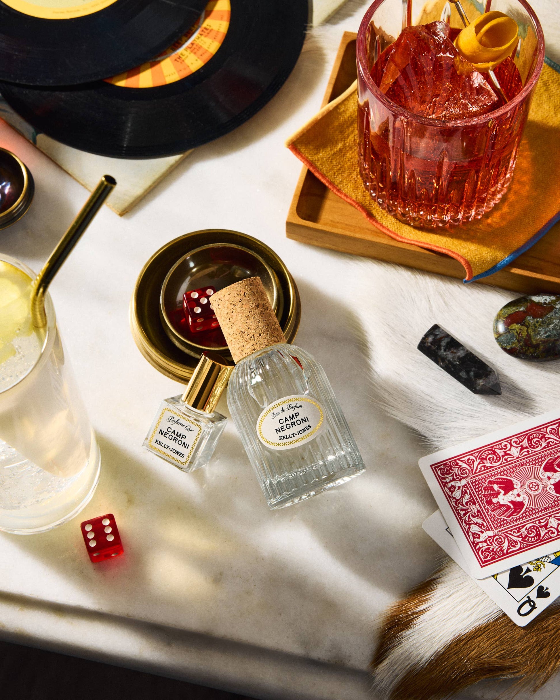 Cocktail glass with a red drink, Campari bottle, playing cards, and dice on a marble surface.