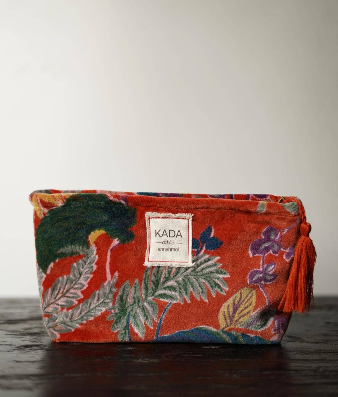 Floral-patterned pouch with tassel on a wooden surface, featuring the brand 'KADA'.