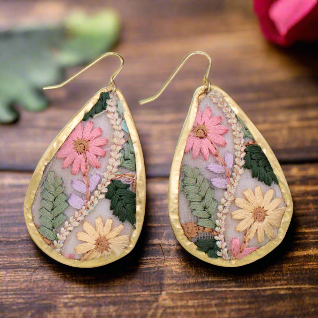 Teardrop-shaped earrings with floral designs on a wooden surface