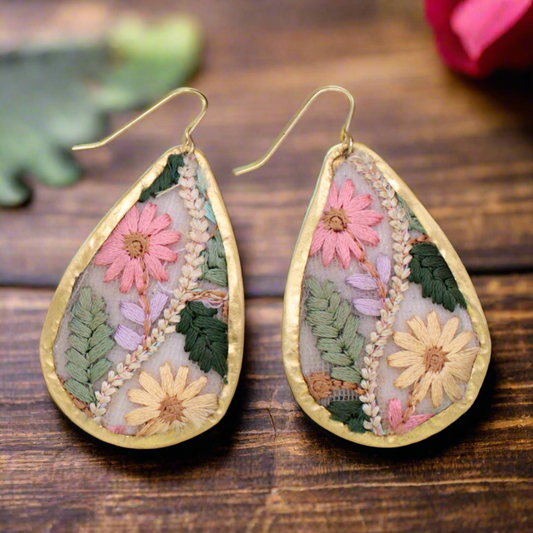 Teardrop-shaped earrings with floral designs on a wooden surface