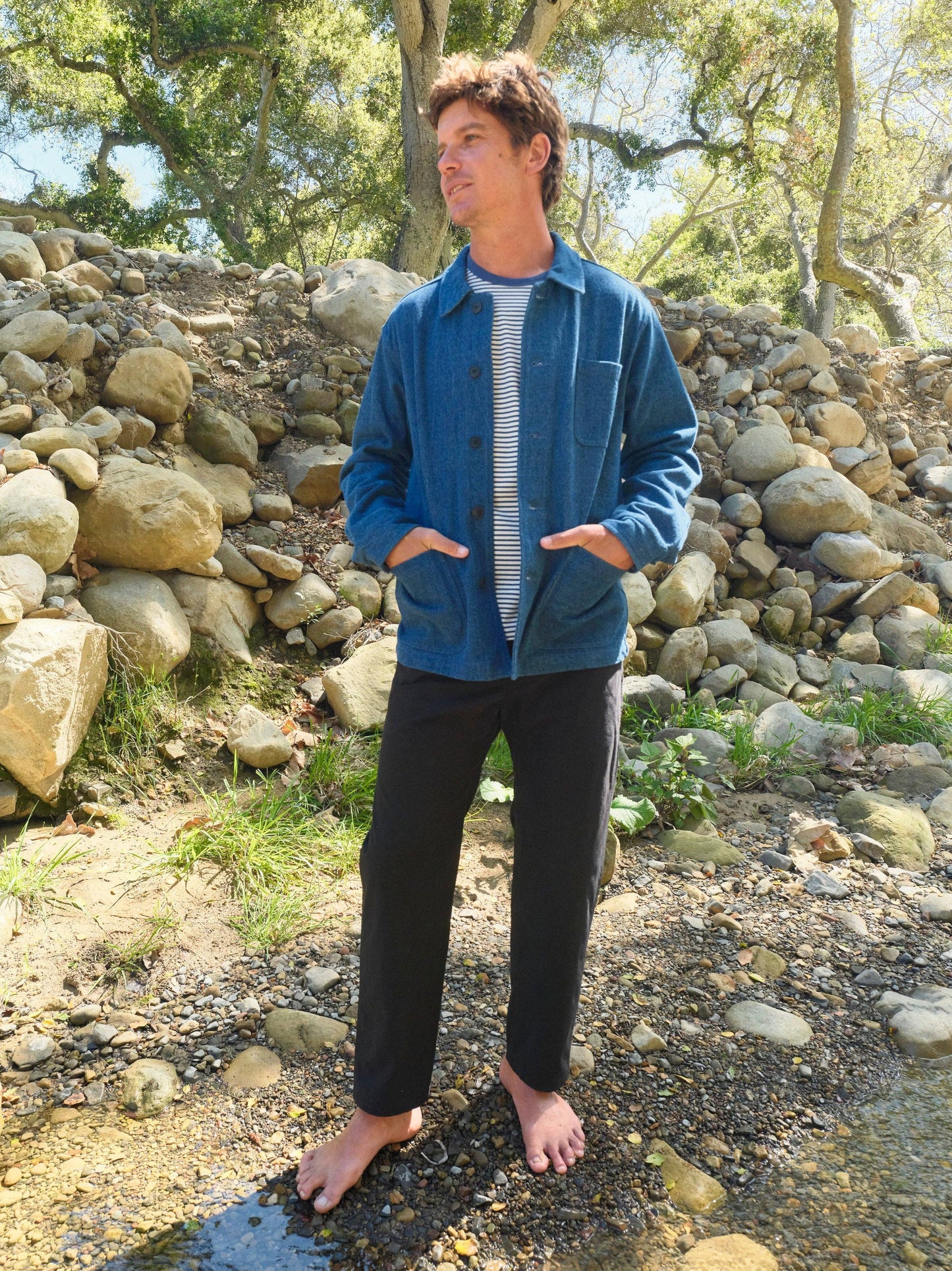 Person wearing a blue jacket and black pants standing in a natural setting with rocks and trees.
