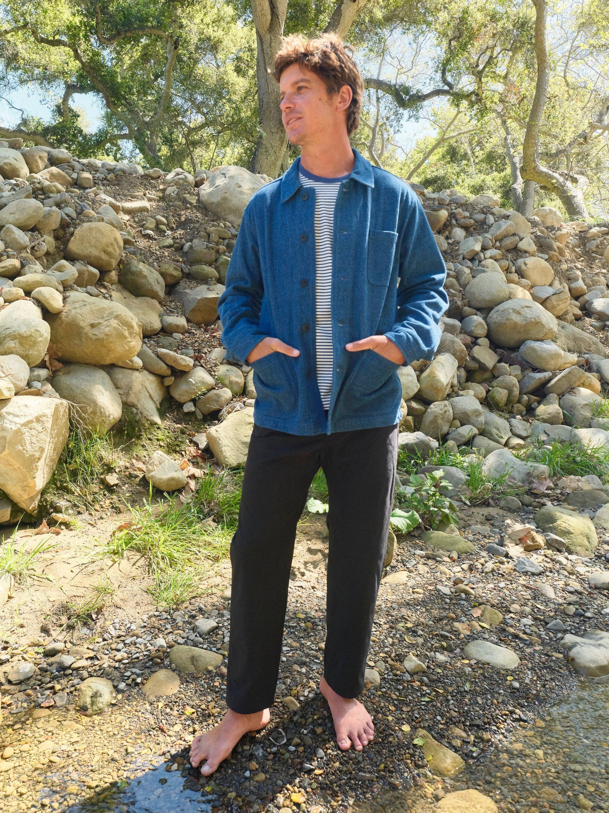 Person wearing a blue jacket and black pants standing in a natural setting with rocks and trees.