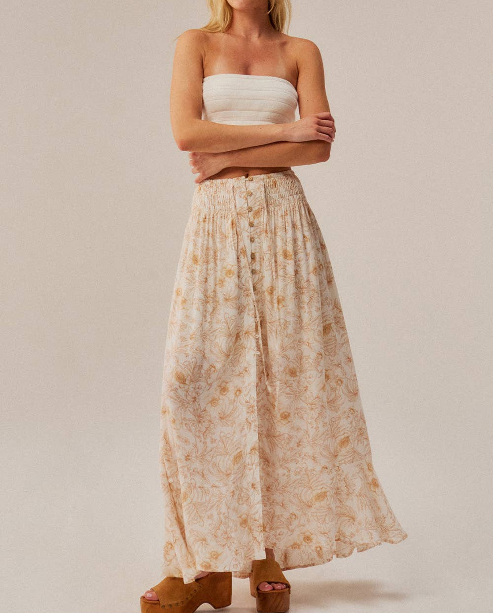Woman wearing a strapless top and floral skirt on a beige background
