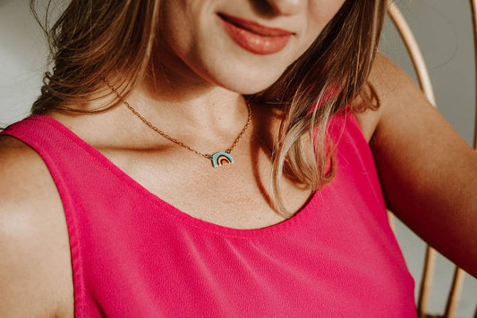 Person wearing a pink sleeveless top and a necklace with a rainbow pendant.