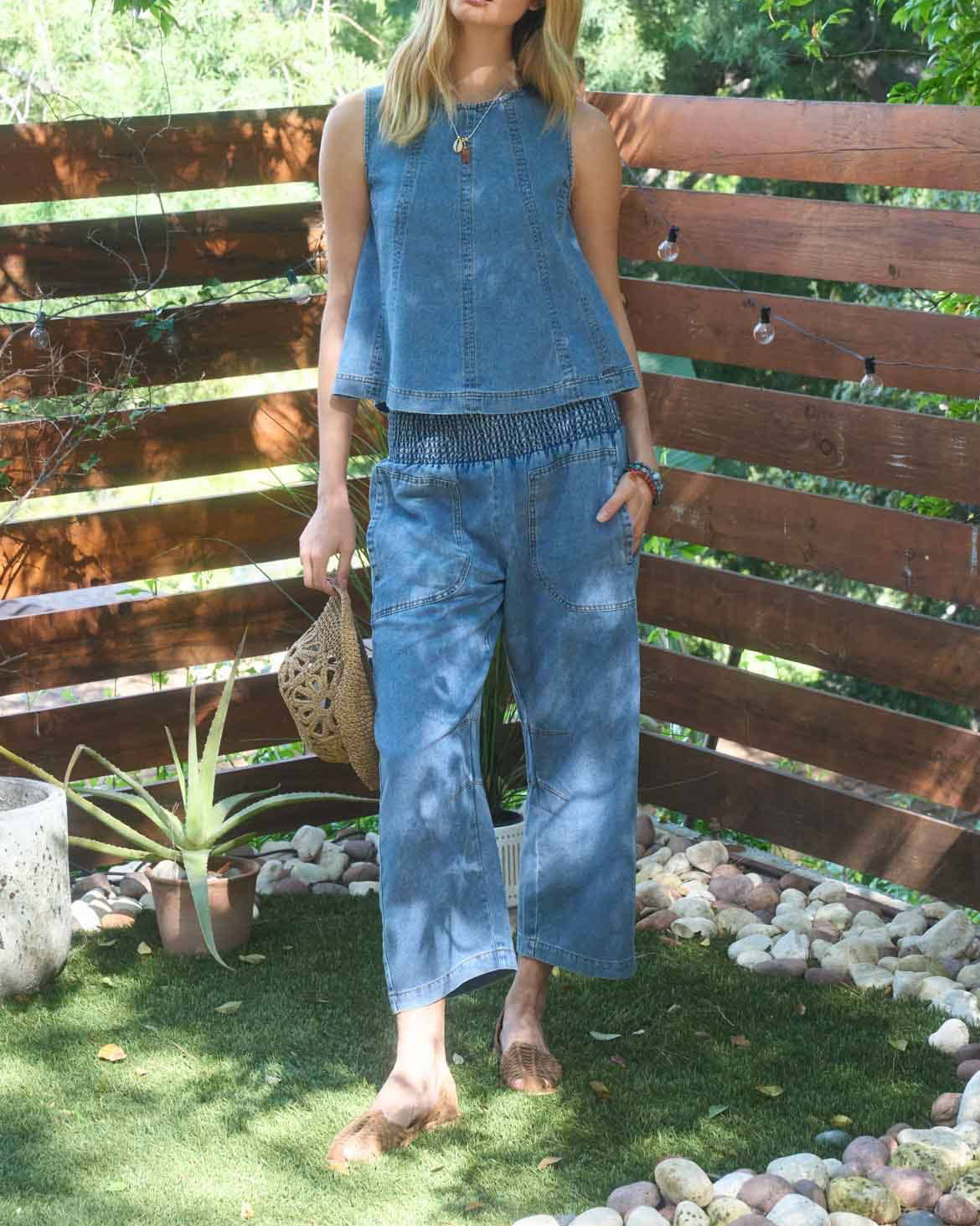 Woman in a blue outfit standing in a garden with a wooden fence and greenery.