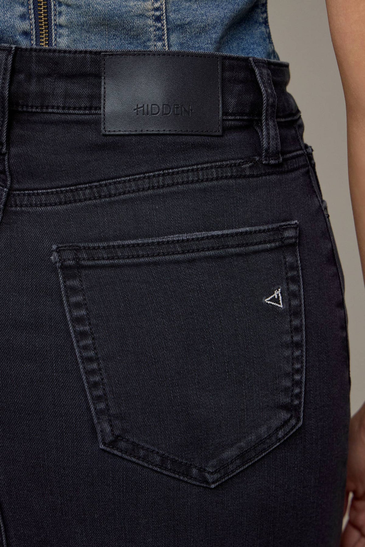 Close-up of black jeans with a brand label on a neutral background