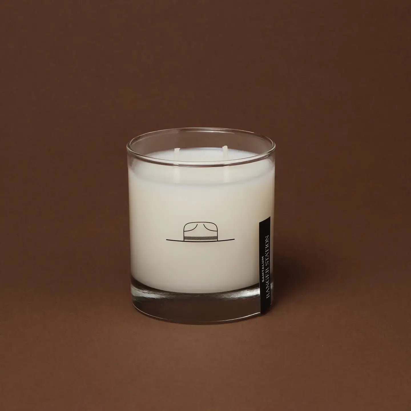 White candle in a glass jar with a label on a brown background