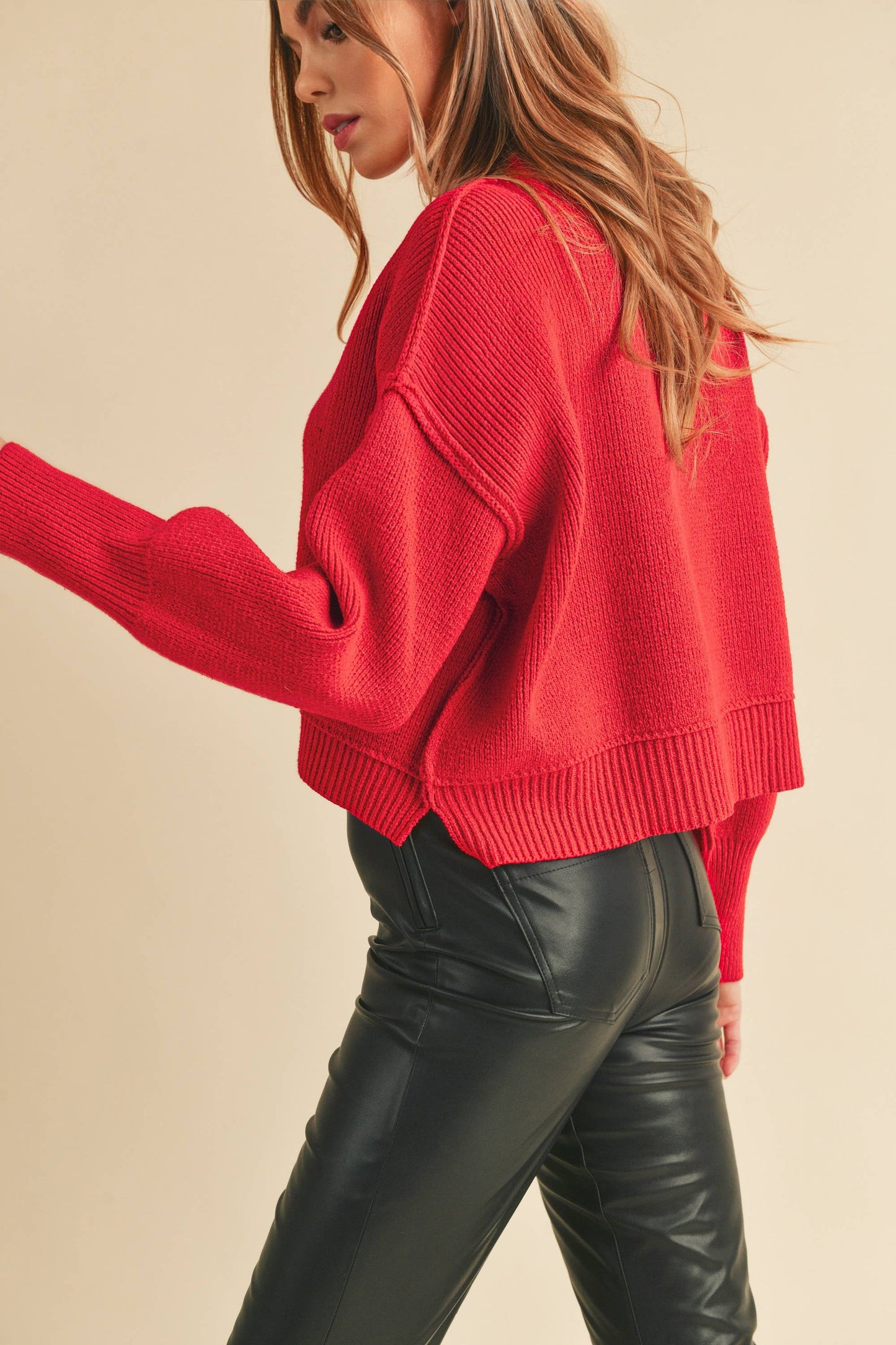 Woman wearing a red sweater and black leather pants on a beige background