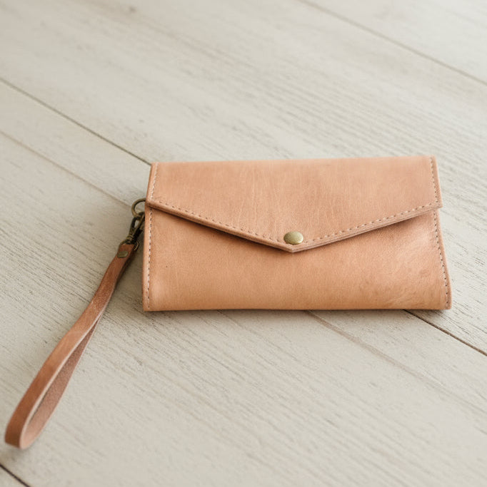 Tan leather wallet with wrist strap on a light wooden surface