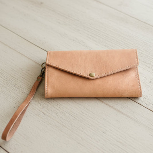 Tan leather wallet with wrist strap on a light wooden surface
