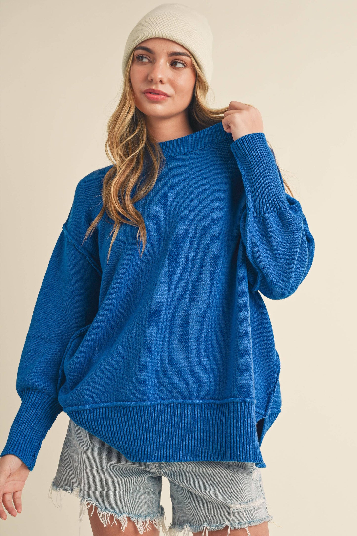 Woman wearing a blue sweater and white beanie on a beige background