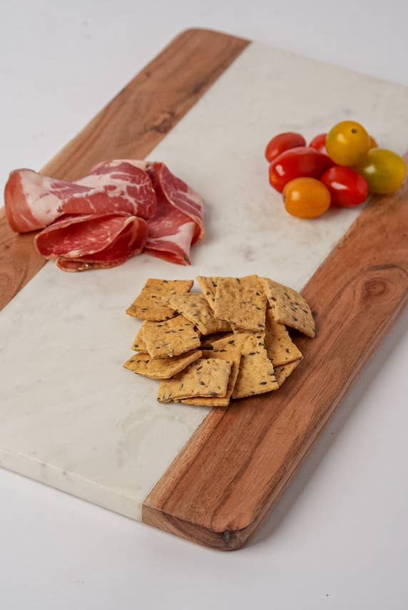 Wooden cutting board with cured meat, crackers, and cherry tomatoes on a white surface