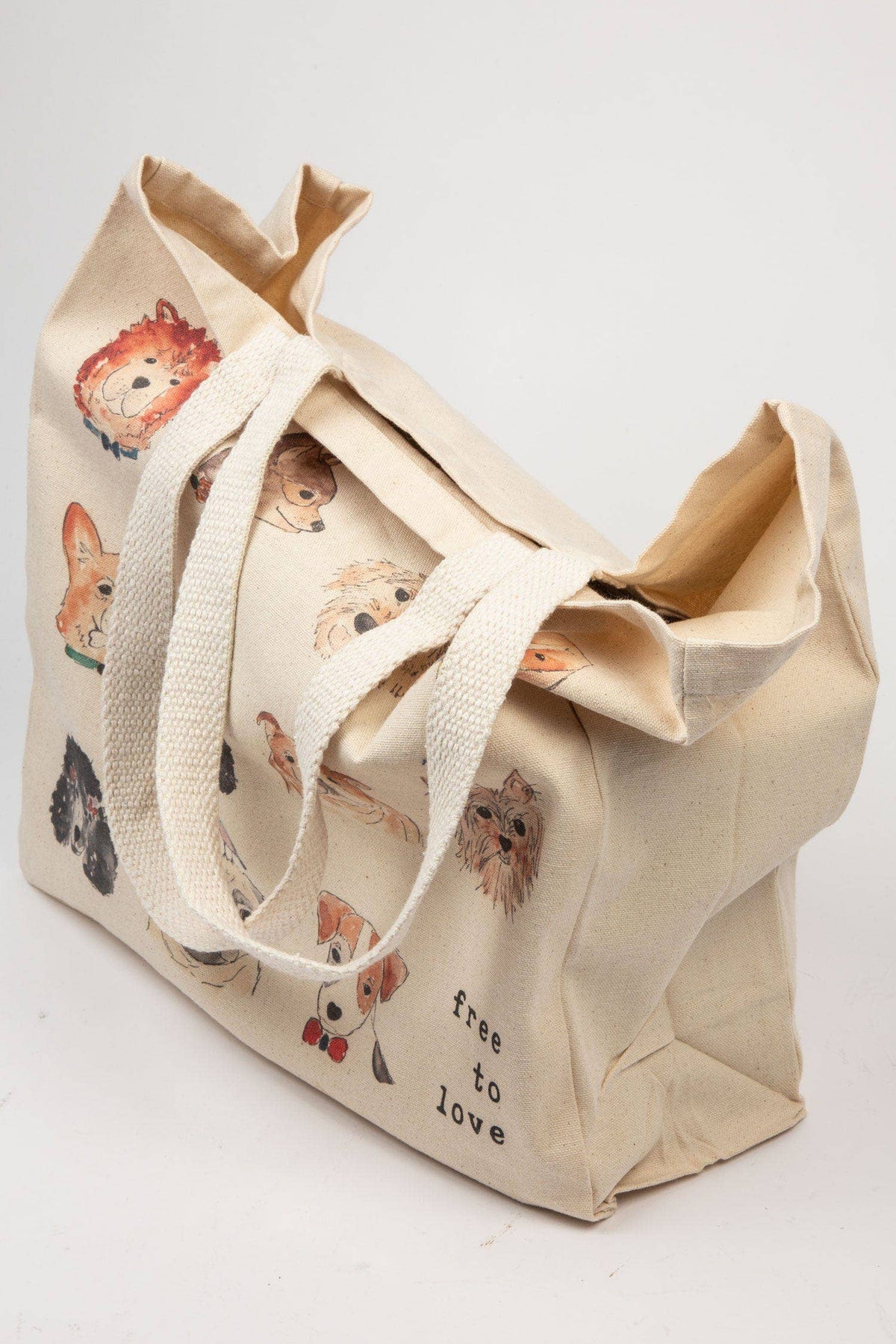 A beige canvas tote bag with printed dog illustrations and the words 'free to love' on the front, shown on a plain light background.