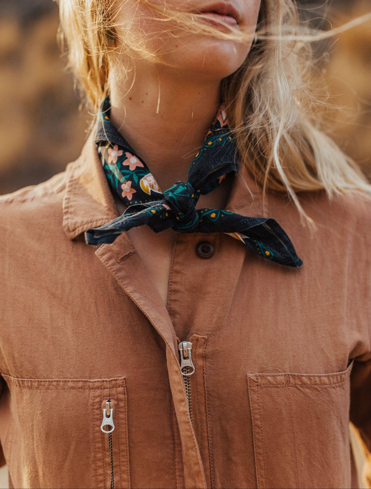 Person wearing a brown jacket with a floral scarf around their neck, outdoors.