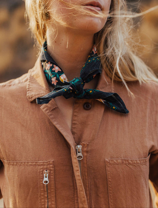 Person wearing a brown jacket with a floral scarf around their neck, outdoors.