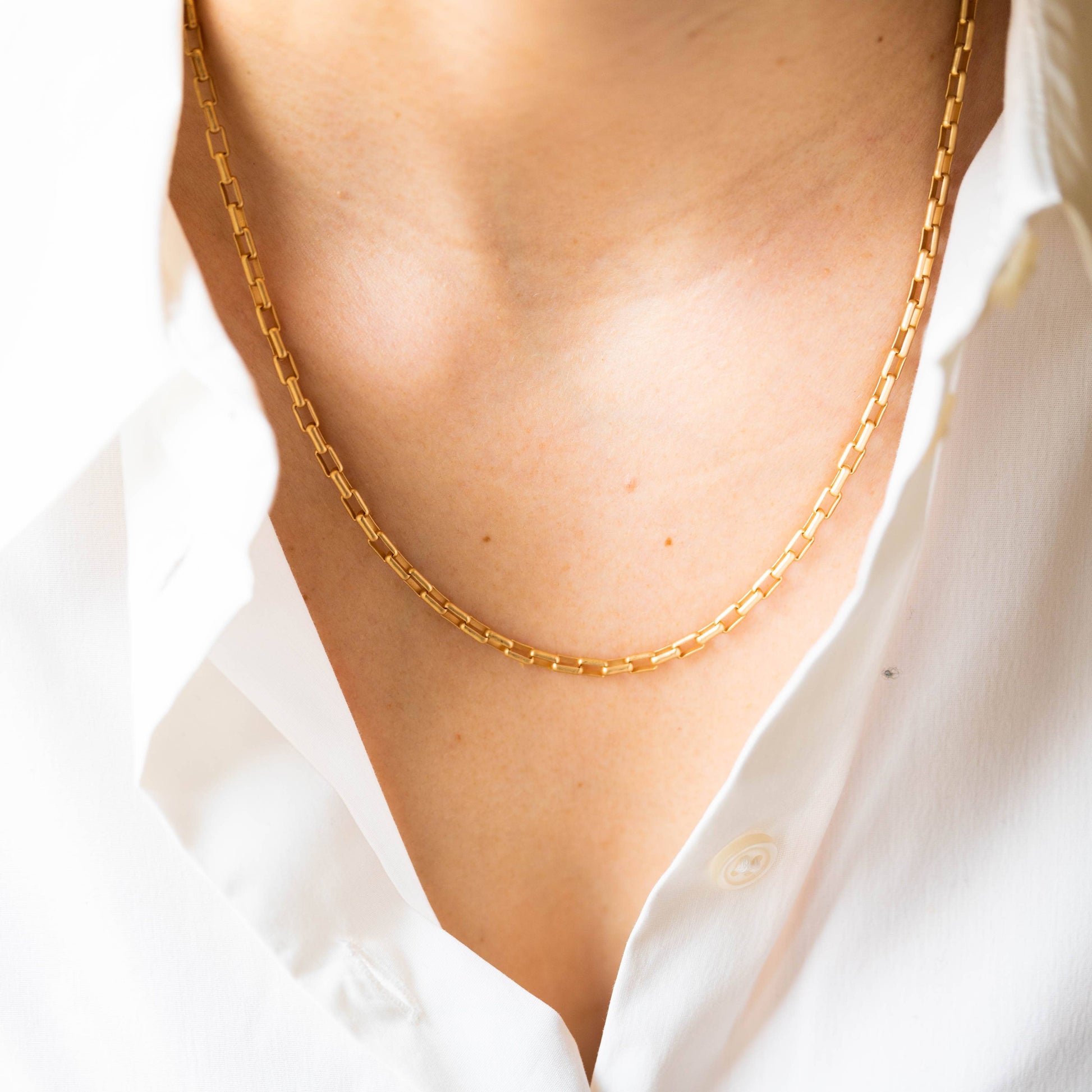 Gold chain necklace worn by a person with a white shirt