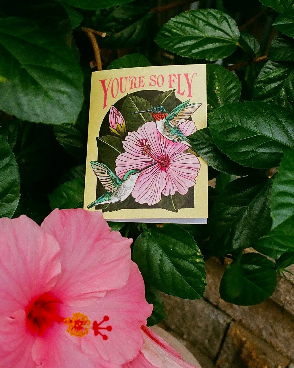 Card with hummingbirds and flowers surrounded by pink flowers and green leaves