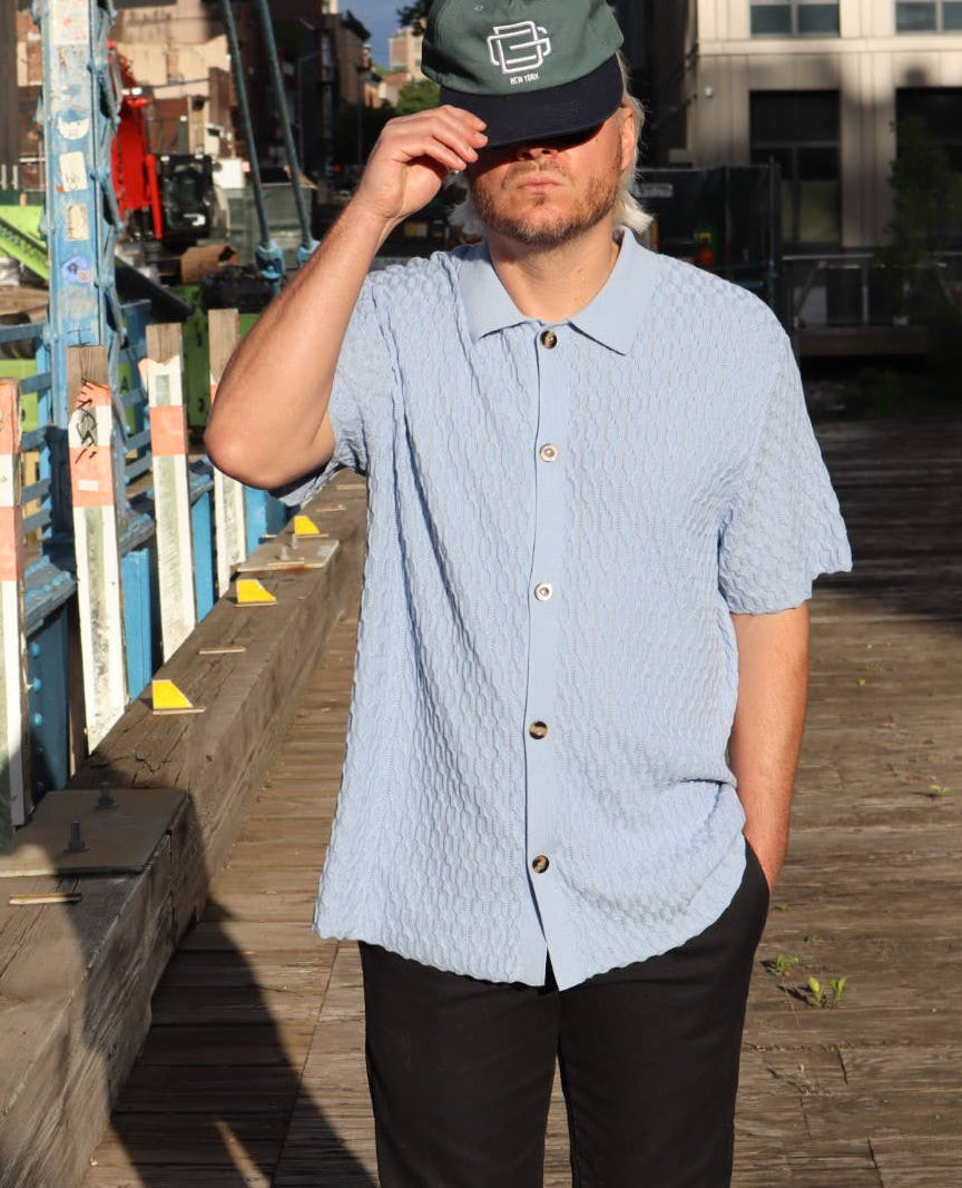 Man wearing a light blue shirt and dark pants on a wooden dock.