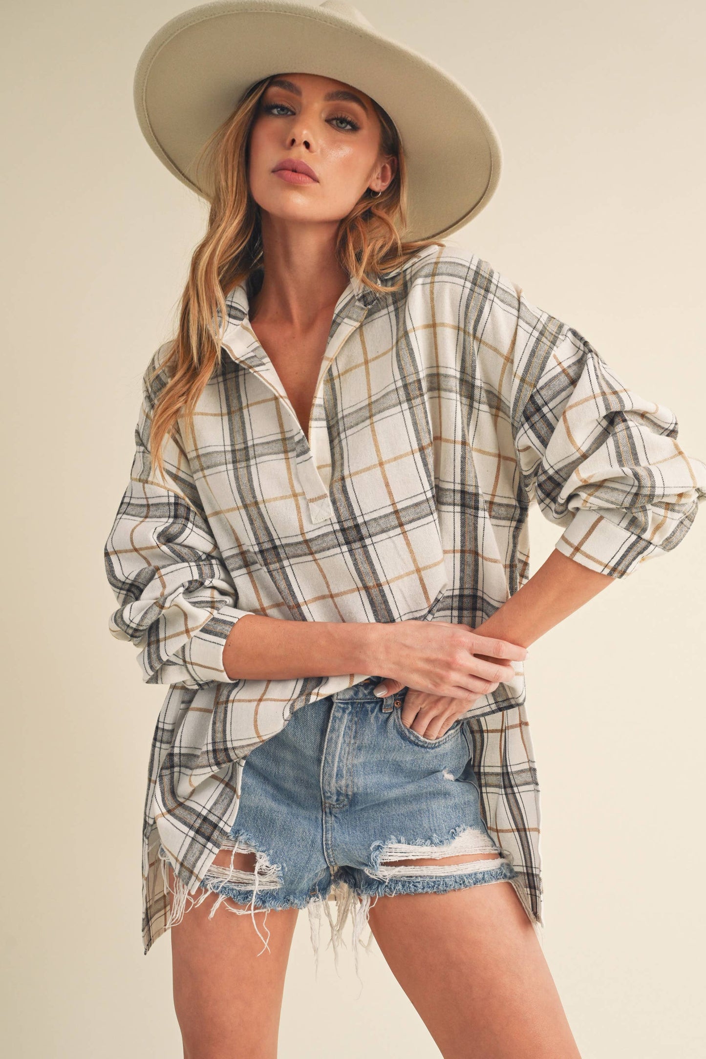 Woman wearing a plaid shirt and denim shorts with a wide-brimmed hat on a plain background