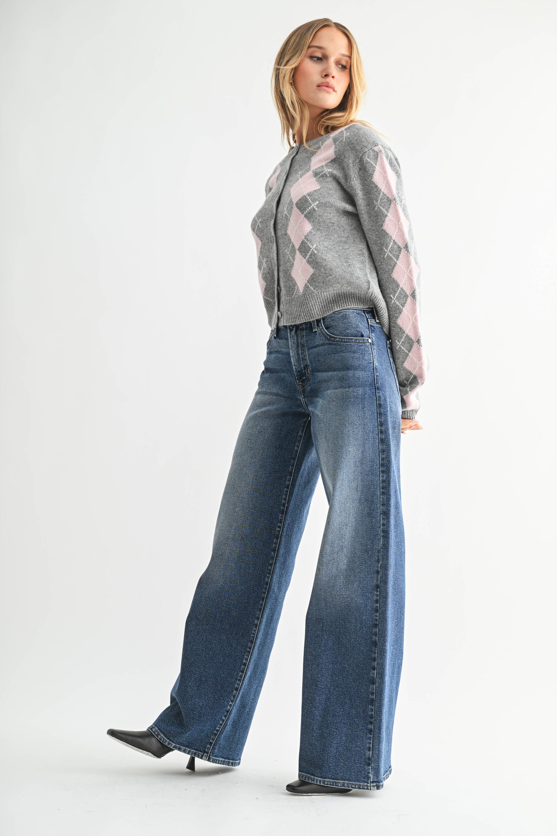 Woman wearing a gray argyle sweater and blue jeans on a white background