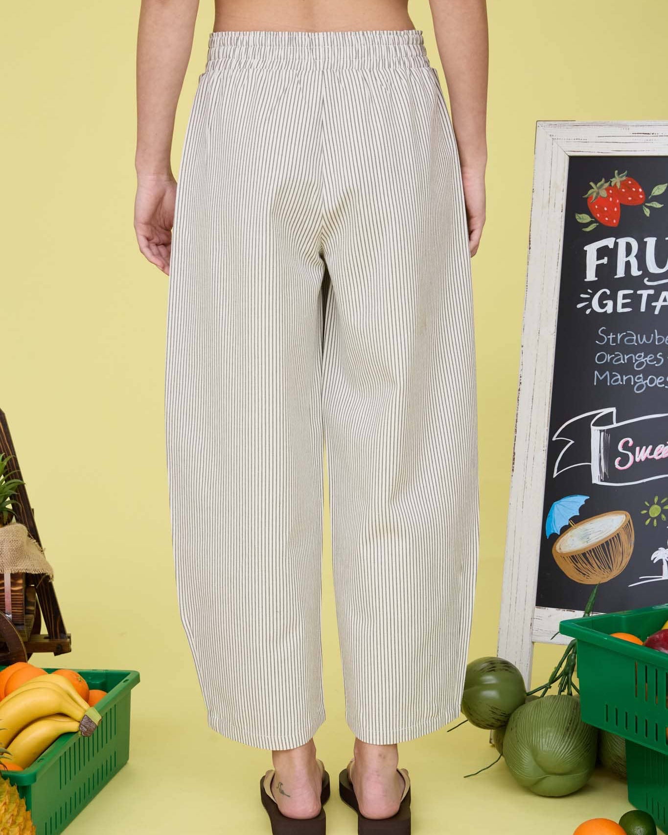 Person wearing light-colored striped pants standing in a kitchen with fruits and a chalkboard menu.