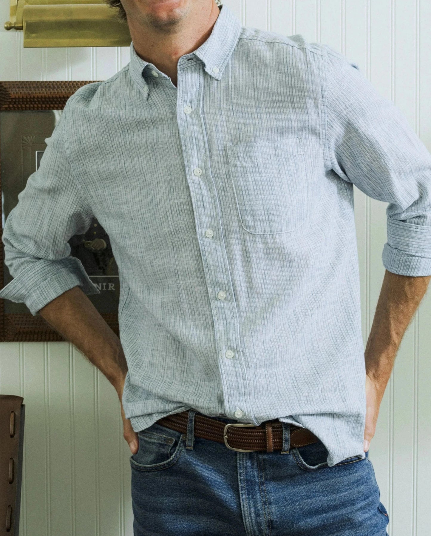 Man wearing a light blue checkered shirt and jeans standing indoors.