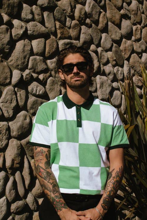 Man wearing a green and white checkered shirt against a stone wall.