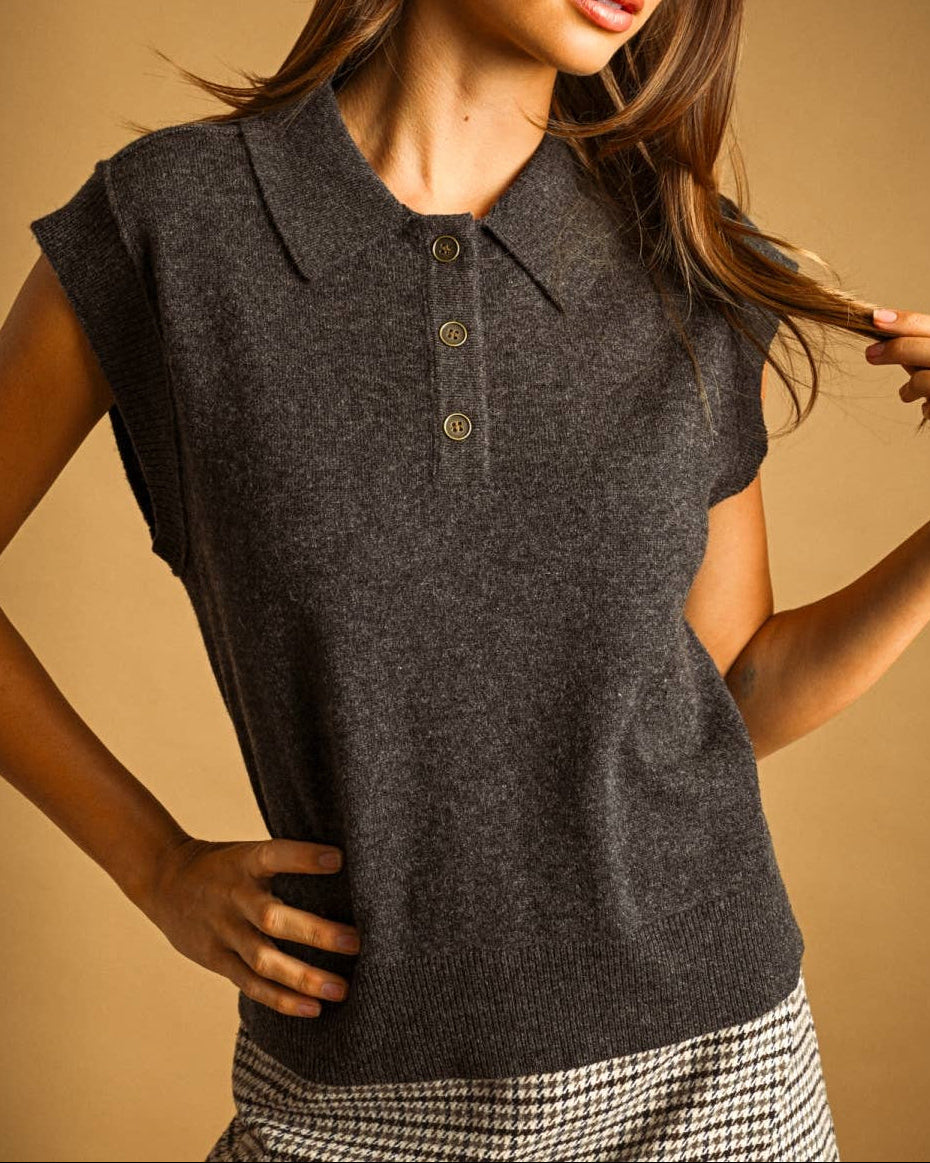 A woman wearing a dark gray sleeveless knit polo shirt with a three-button placket, posed against a warm beige studio background.