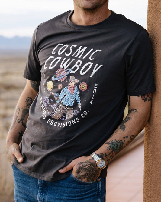 Man wearing a black t-shirt with 'Cosmic Cowboy' design, standing against a desert backdrop.