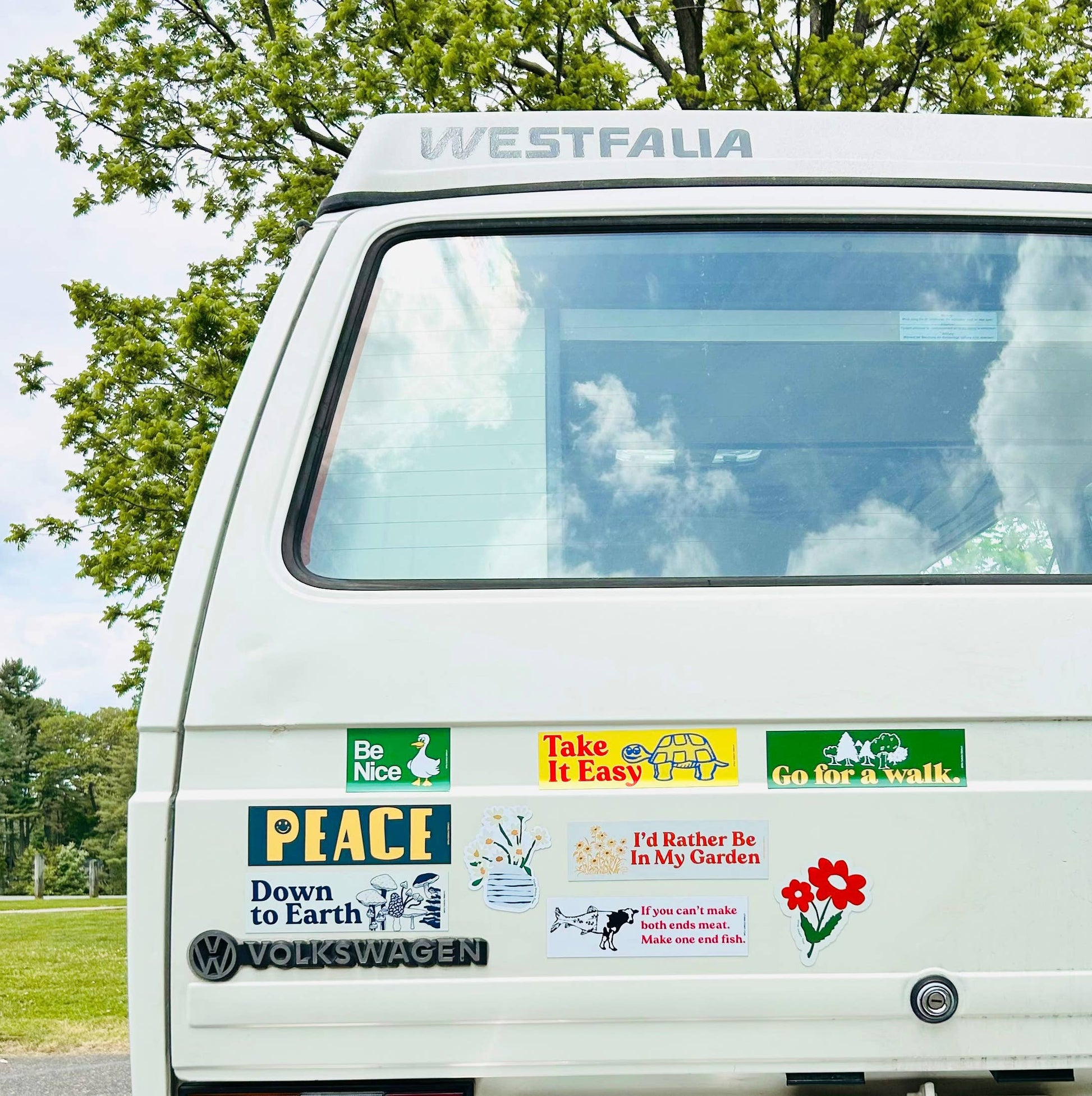 White Westfalia van with various bumper stickers on a road trip with trees in the background