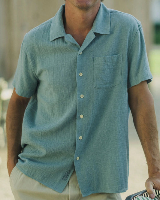 Man wearing a light blue shirt standing outdoors with blurred background