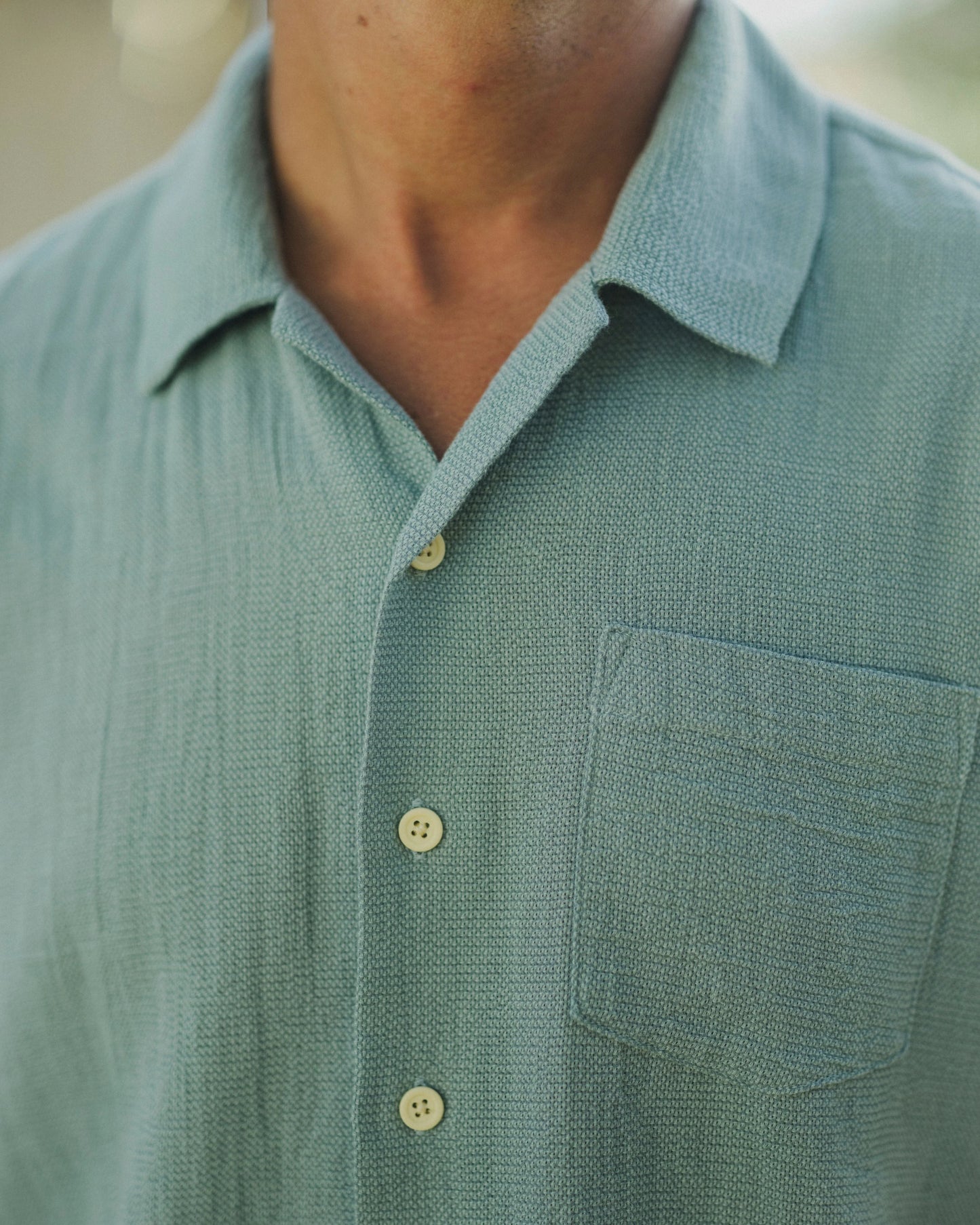 Close-up of a person wearing a green textured shirt with buttons and a pocket.
