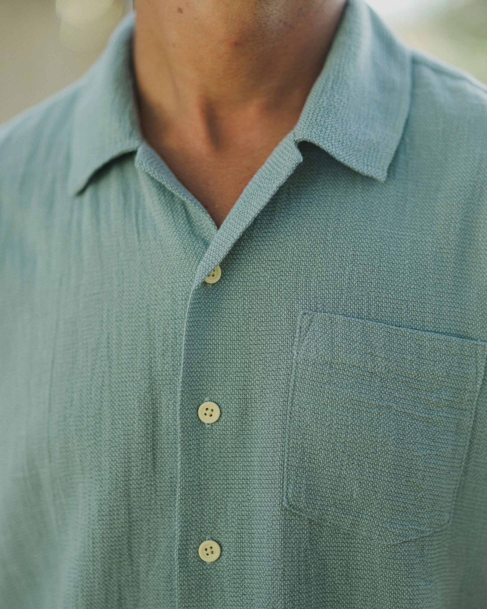 Close-up of a person wearing a green textured shirt with buttons and a pocket.