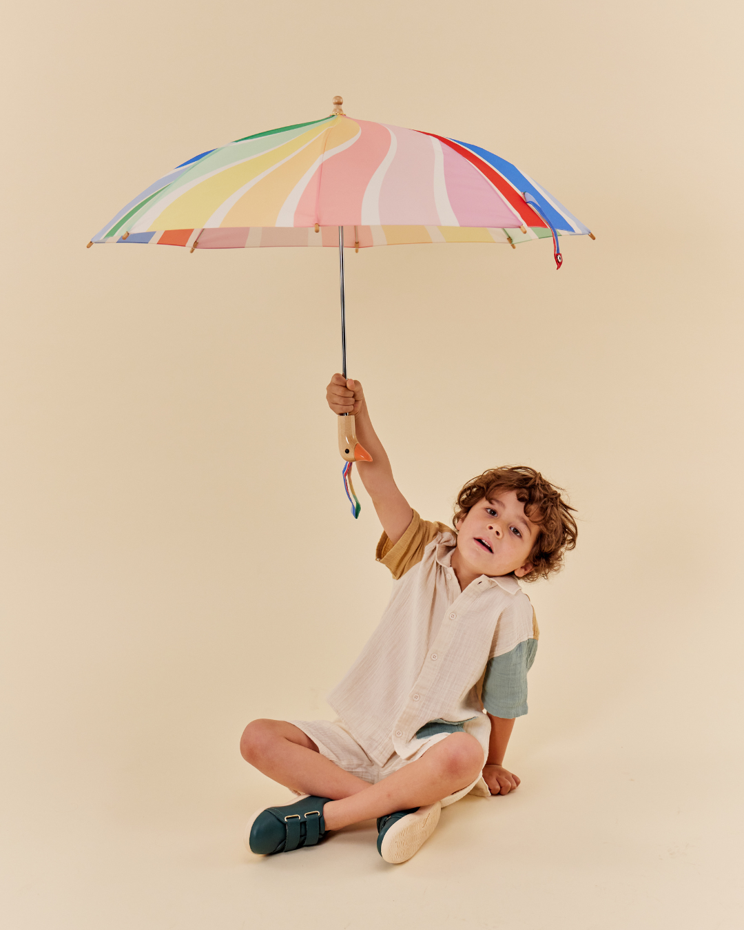 Child holding a colorful striped umbrella against a beige background