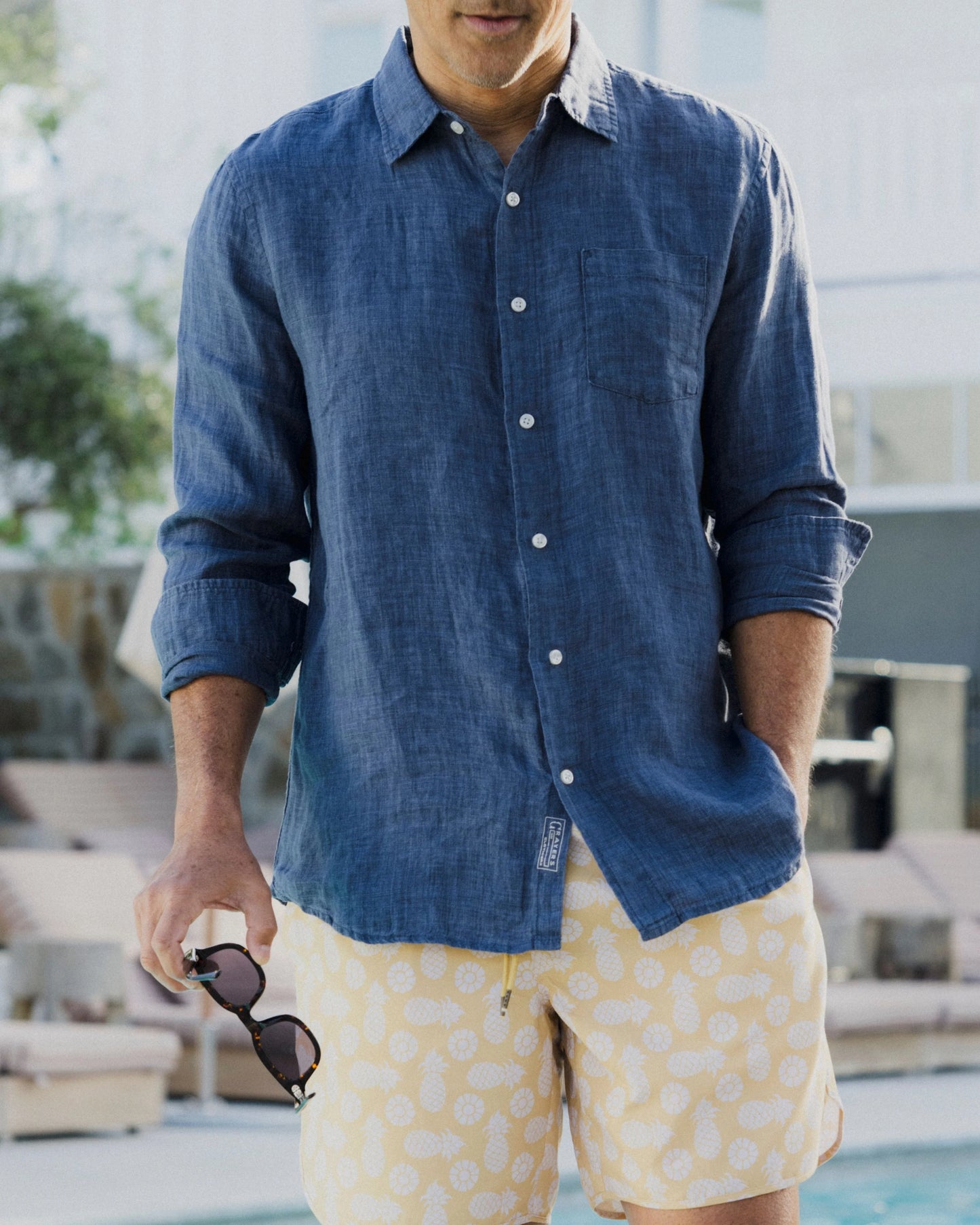 Man wearing a blue shirt and yellow patterned shorts by a pool.