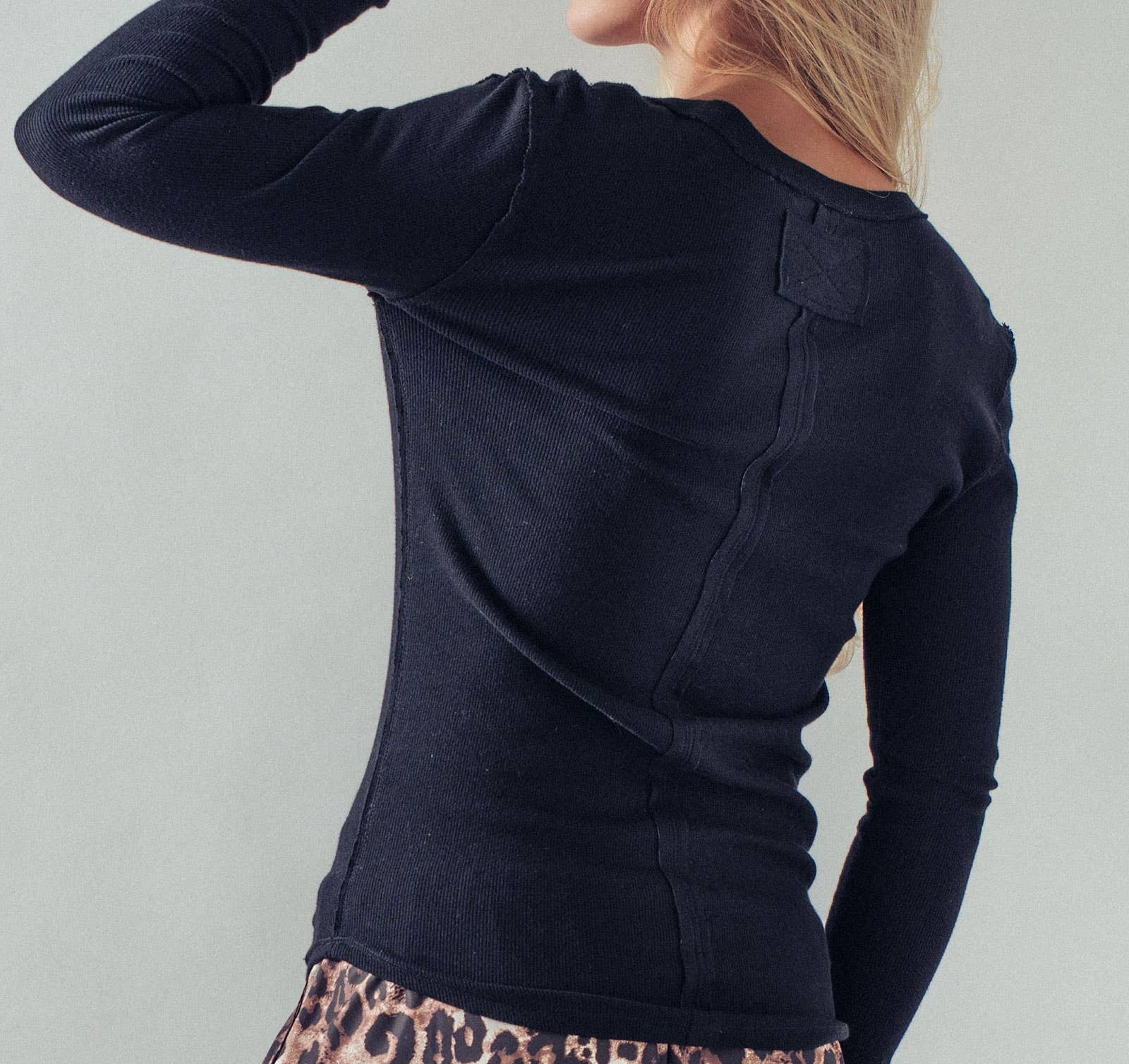 Person wearing a black long-sleeve top and leopard print pants against a light gray background