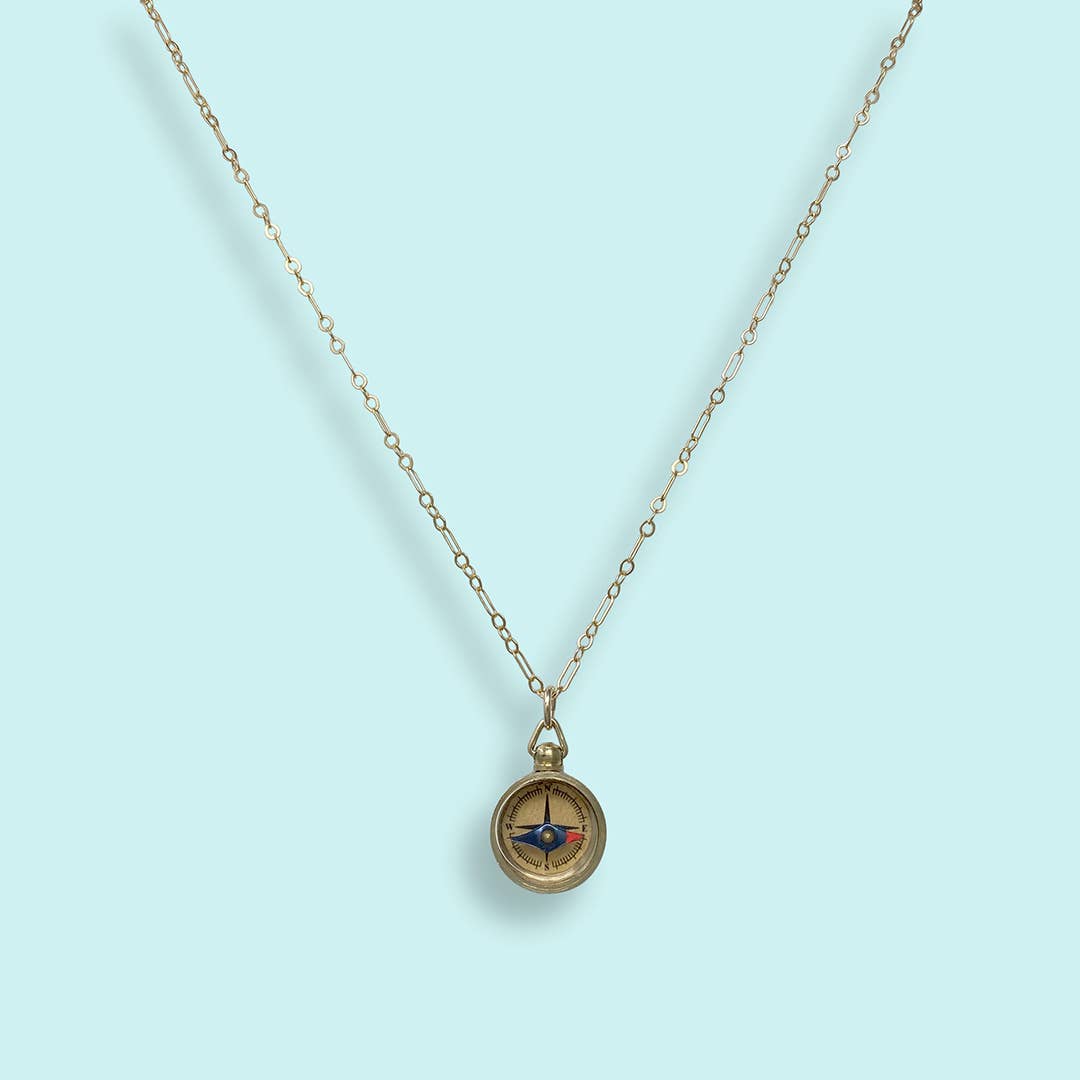 Gold necklace with a compass pendant on a light blue background