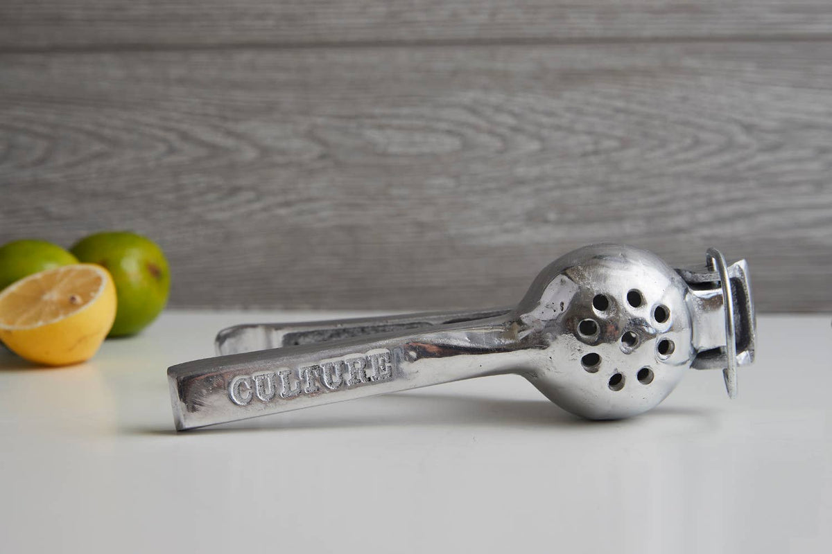 Metallic garlic press on a light surface with lemons and limes in the background