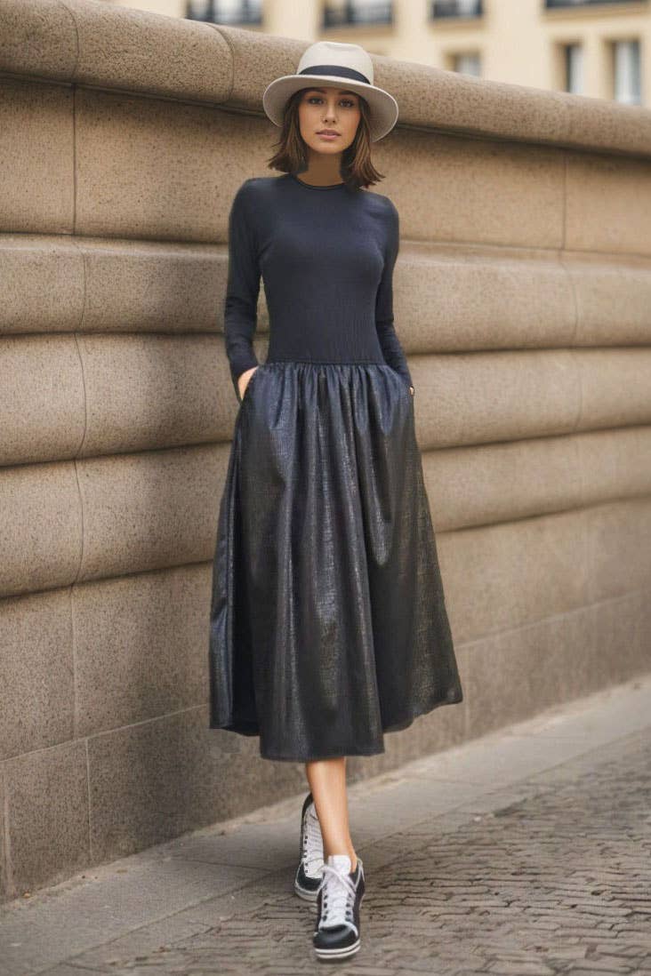 Woman wearing a navy long-sleeve top and black leather skirt against a stone wall.
