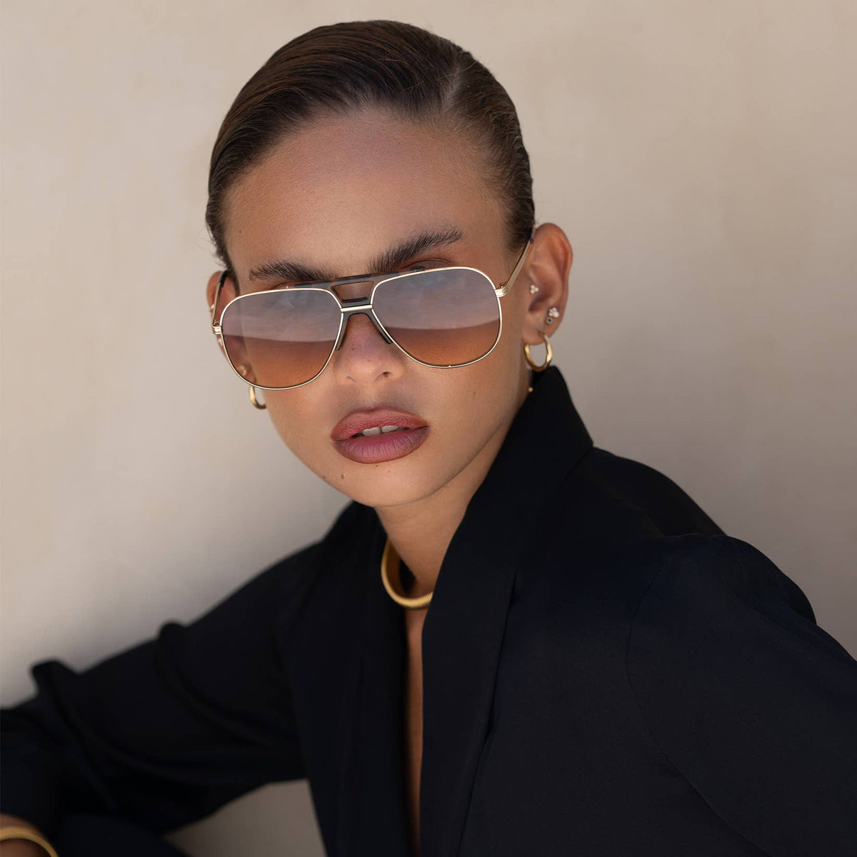 Person wearing gold aviator sunglasses and a black outfit against a neutral background