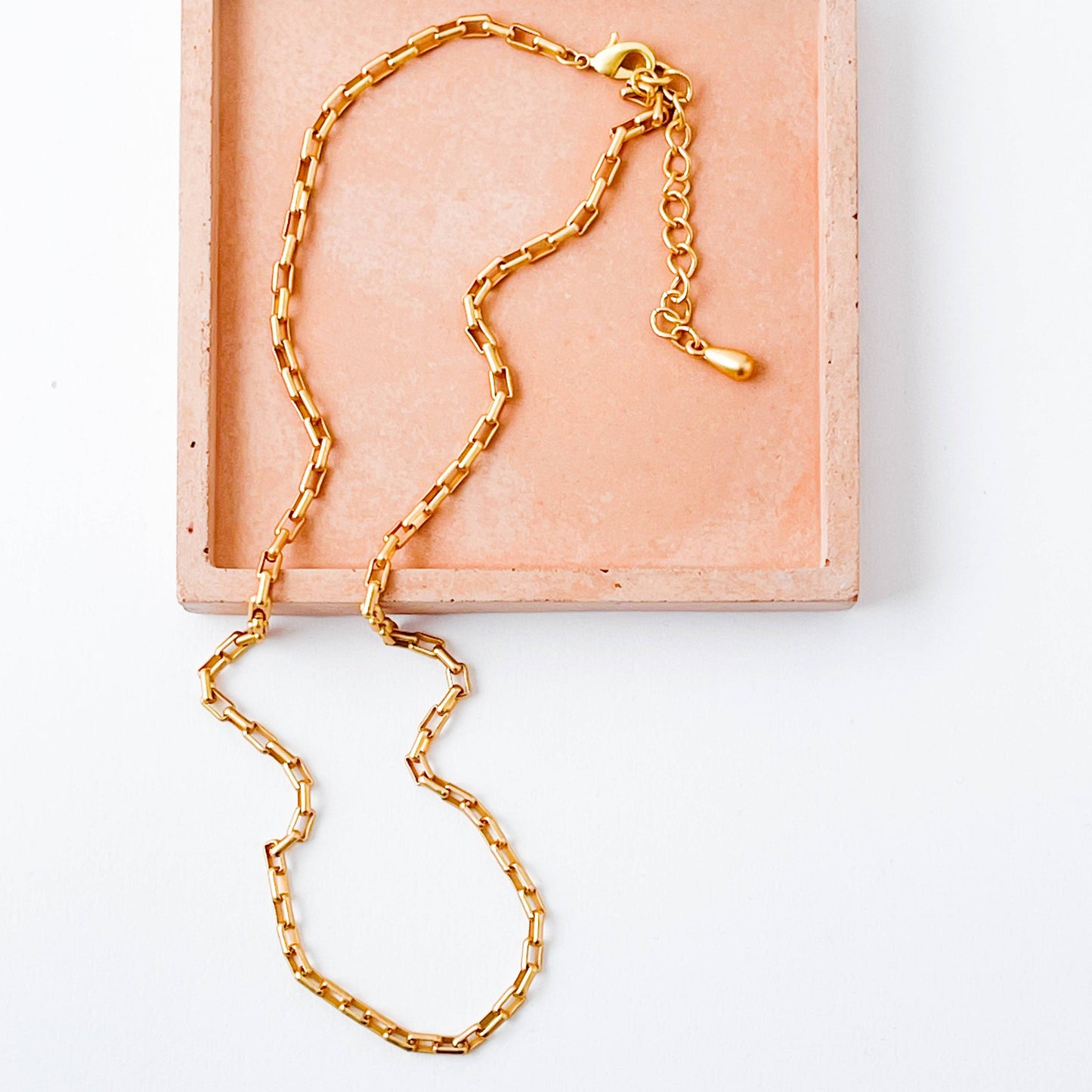 Gold chain necklace on a light pink jewelry box with a white background