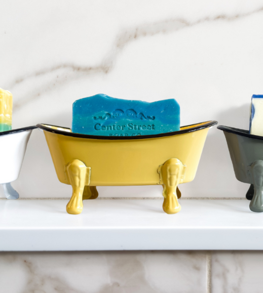Colorful soap holders shaped like bathtubs on a marble countertop.